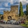 Four vintage luxury cars parked in front of a historic stone castle with a tower, arched entrance and surrounding greenery